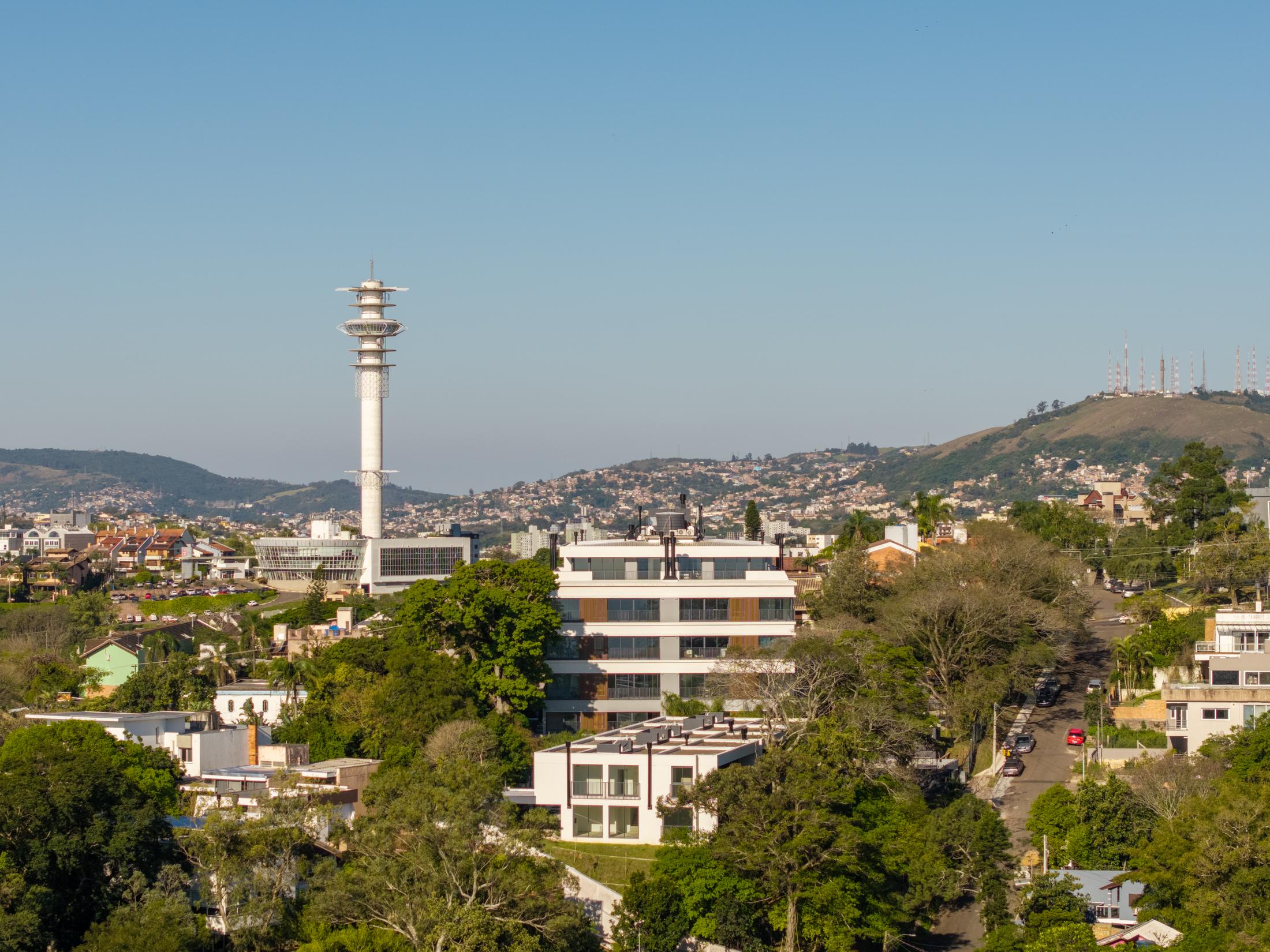 Vista do alto do bairro, com o Aria entre árvores e a torre de TV ao fundo