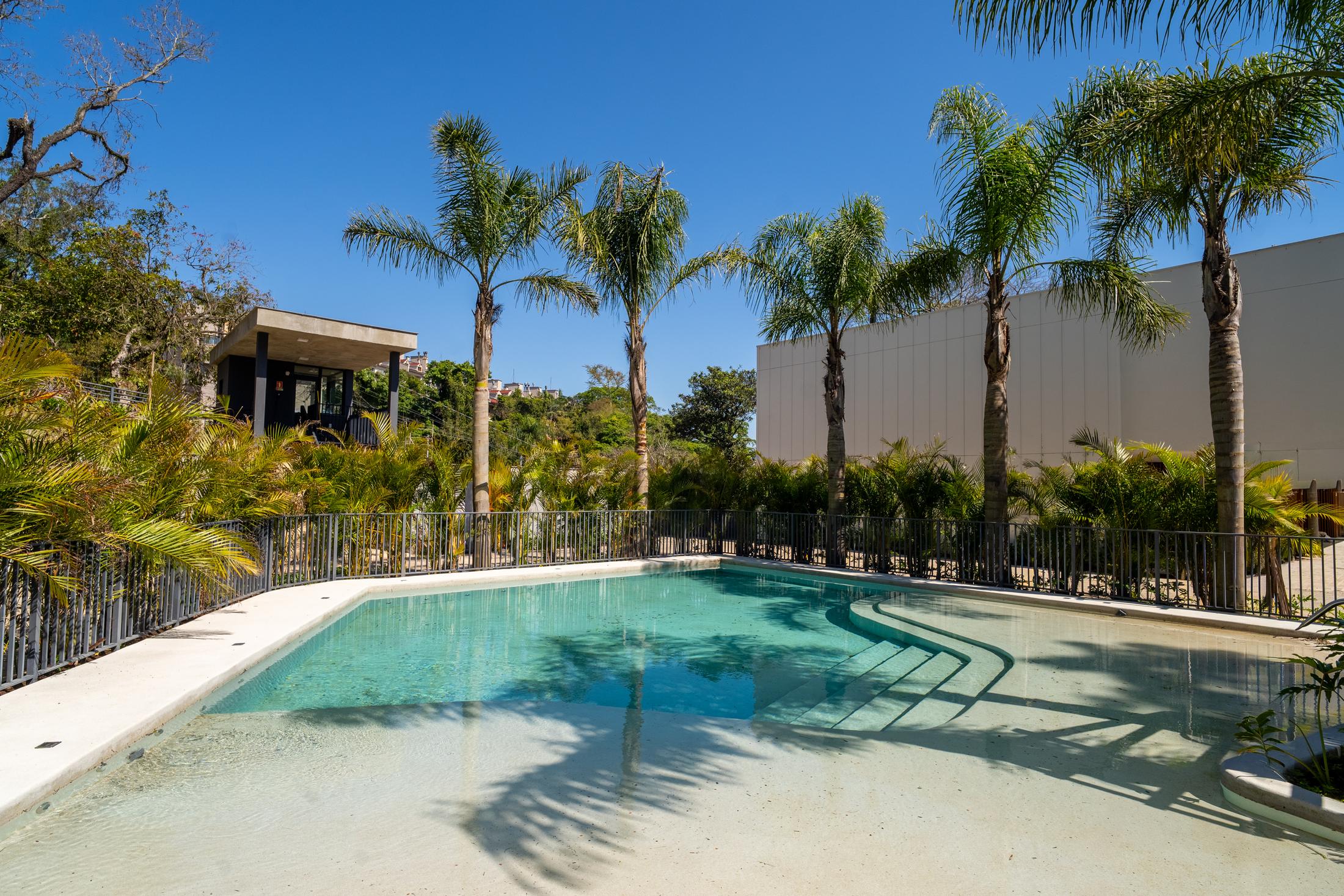 Piscina do Aria com água cristalina, palmeiras e deck claro sob o céu azul
