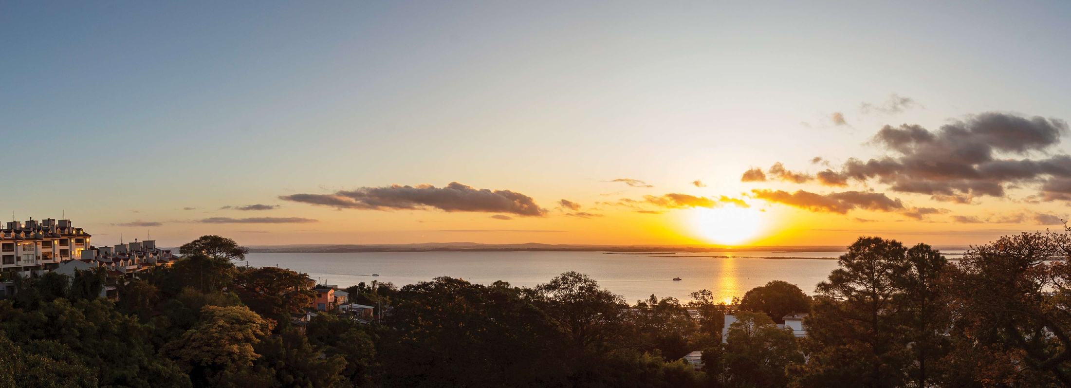 Pôr do sol sobre o Guaíba visto do alto, com a mata em primeiro plano