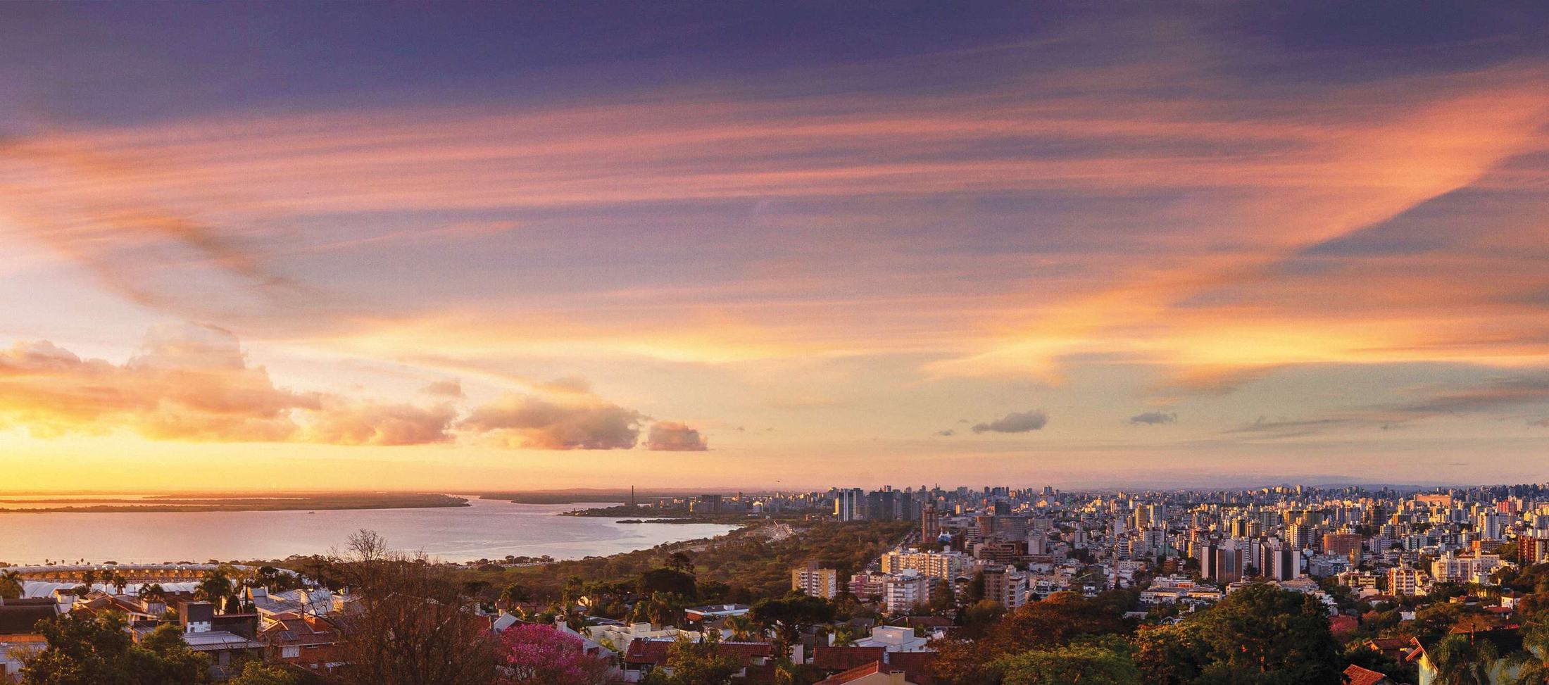 Panorama de Porto Alegre ao entardecer visto do terreno do Aria, com o Guaíba e o céu rosado
